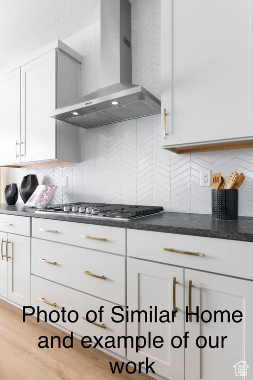 Kitchen featuring white cabinetry, light wood-type flooring, backsplash, and wall chimney range hood