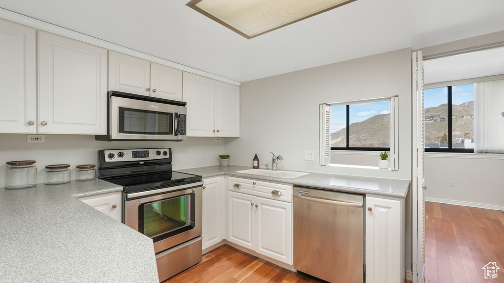 Kitchen featuring appliances with stainless steel finishes, white cabinetry, sink, and light wood-type flooring