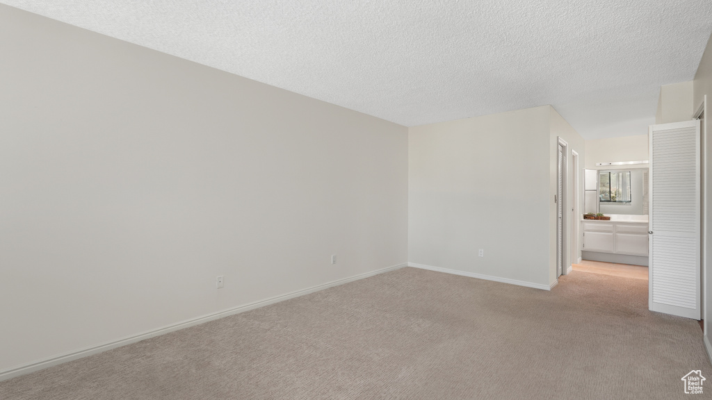Unfurnished bedroom featuring light colored carpet, ensuite bath, and a textured ceiling