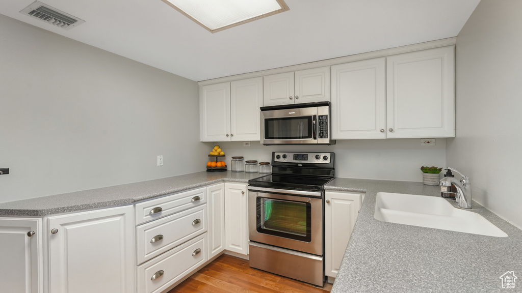 Kitchen with appliances with stainless steel finishes, light wood-type flooring, white cabinets, and sink