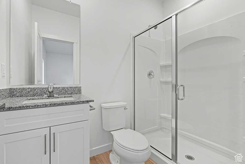 Bathroom with vanity with extensive cabinet space, toilet, hardwood / wood-style flooring, and a shower with door