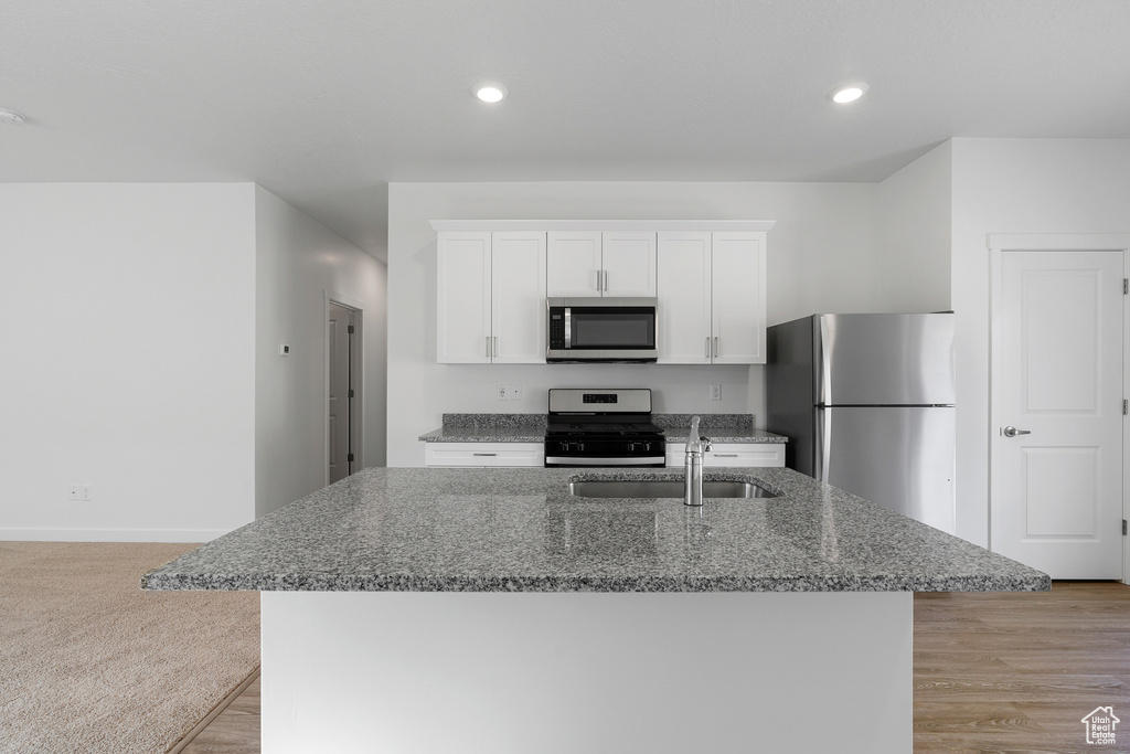 Kitchen with stainless steel appliances, light colored carpet, dark stone counters, white cabinets, and sink