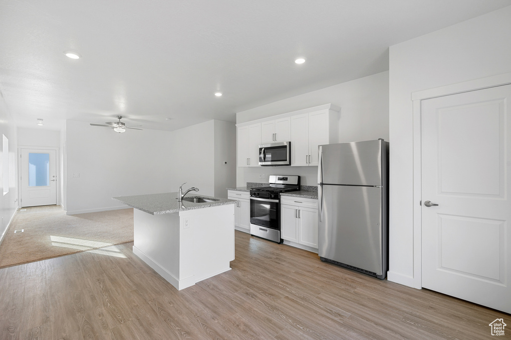 Kitchen featuring white cabinets, appliances with stainless steel finishes, a kitchen island with sink, sink, and ceiling fan