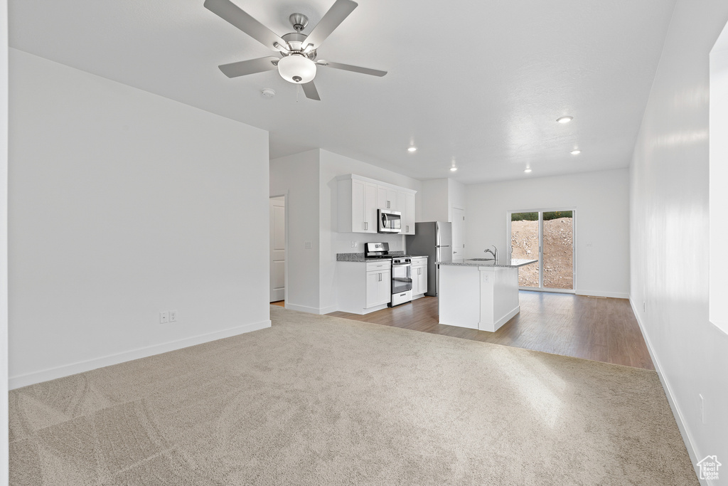 Unfurnished living room featuring dark colored carpet, sink, and ceiling fan