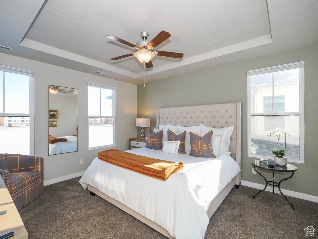 Carpeted bedroom featuring ceiling fan and a raised ceiling