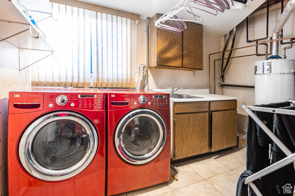 Clothes washing area with washing machine and dryer, light tile floors, cabinets, and sink