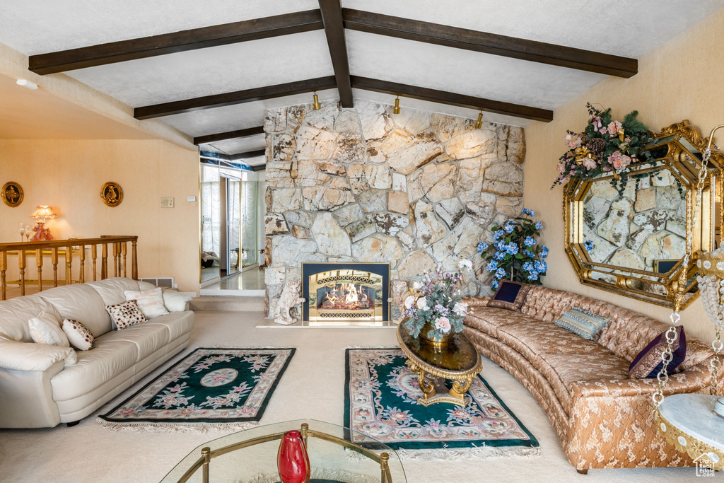 Carpeted living room featuring vaulted ceiling with beams and a stone fireplace