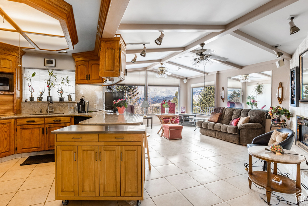 Kitchen featuring tasteful backsplash, light tile floors, a center island, ceiling fan, and vaulted ceiling with beams