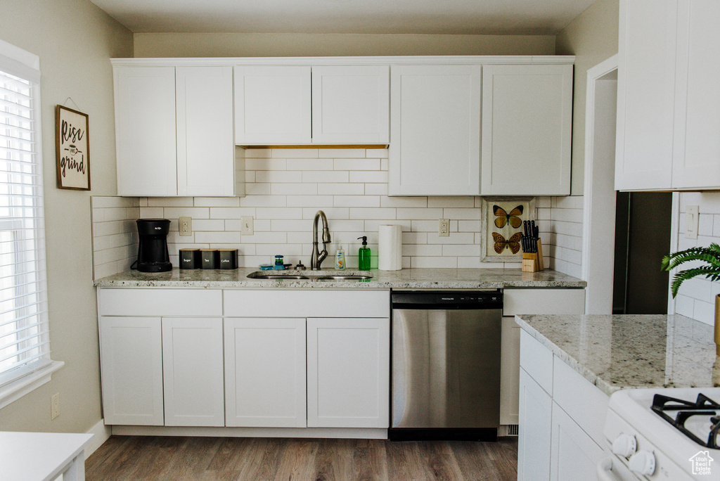 Kitchen featuring white cabinetry, backsplash, stainless steel dishwasher, sink, and wood-type flooring
