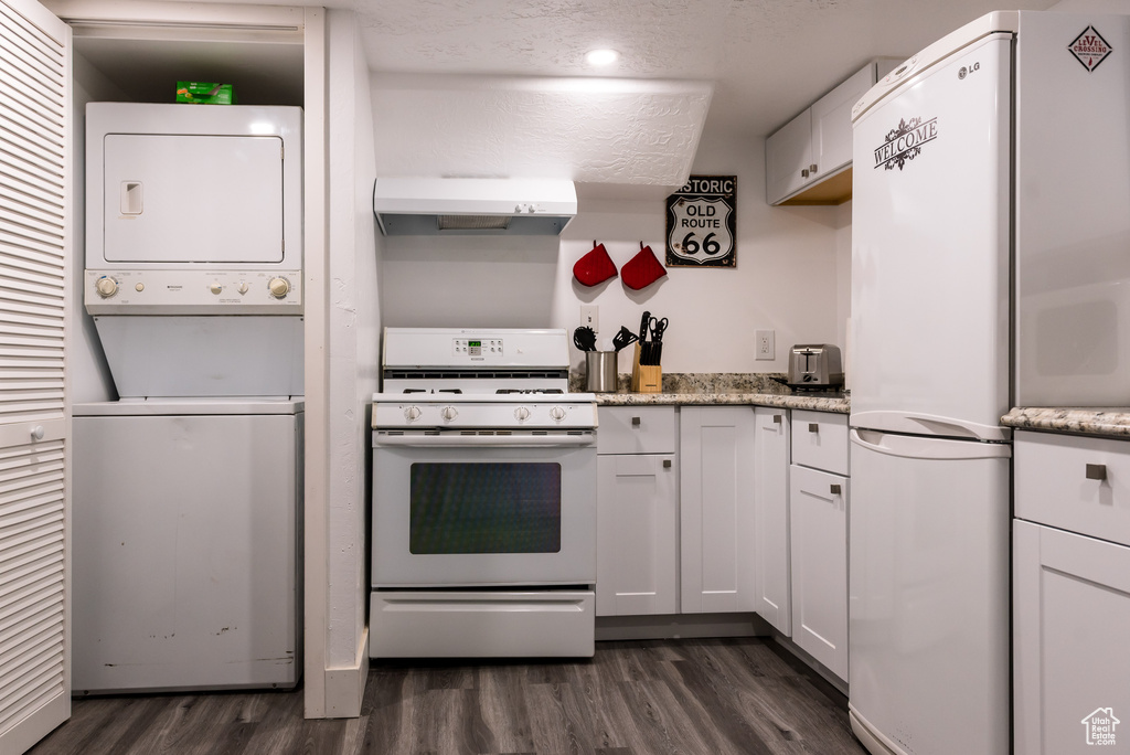 Kitchen with white appliances, dark hardwood / wood-style flooring, stacked washer and clothes dryer, and white cabinets