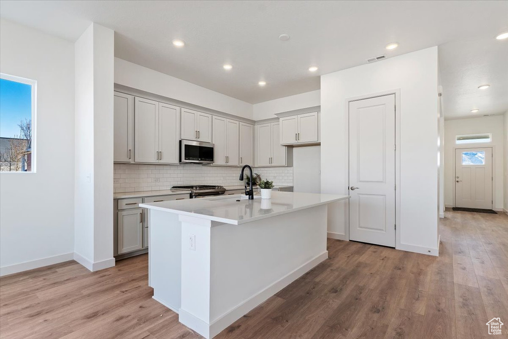 Kitchen featuring light hardwood / wood-style floors, a kitchen island with sink, backsplash, sink, and appliances with stainless steel finishes