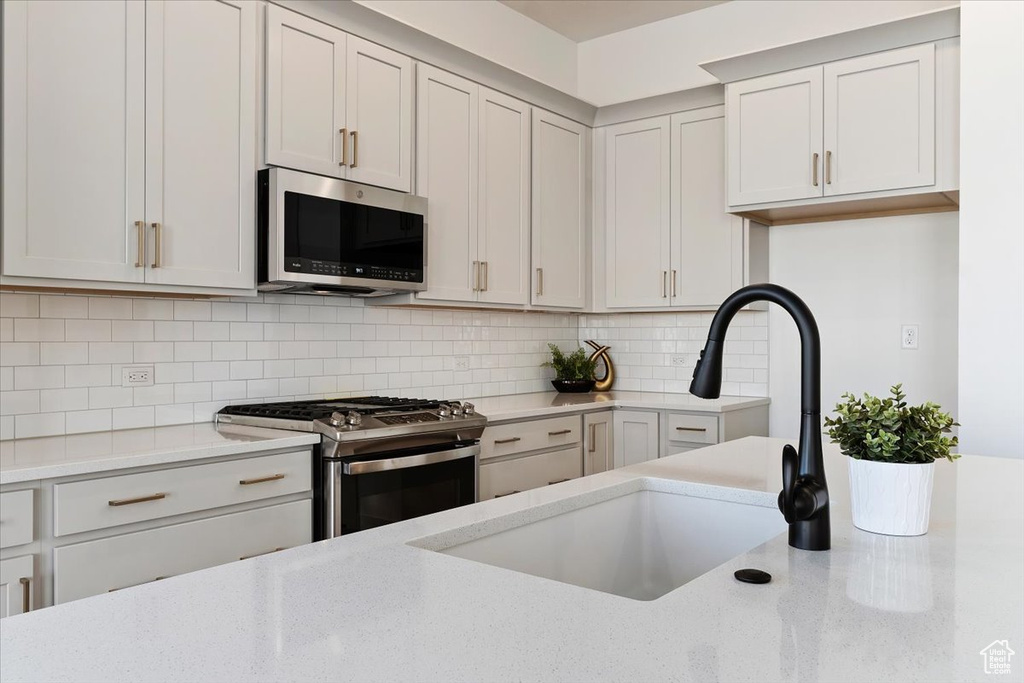 Kitchen with appliances with stainless steel finishes, sink, white cabinets, and tasteful backsplash