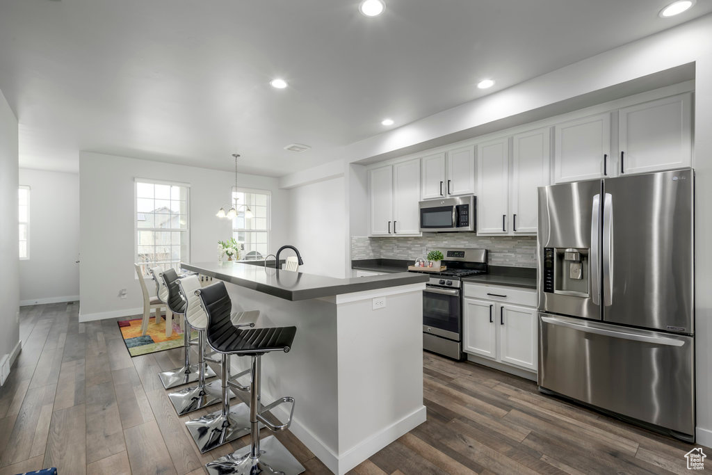 Kitchen with dark wood-type flooring, white cabinetry, a chandelier, backsplash, and appliances with stainless steel finishes