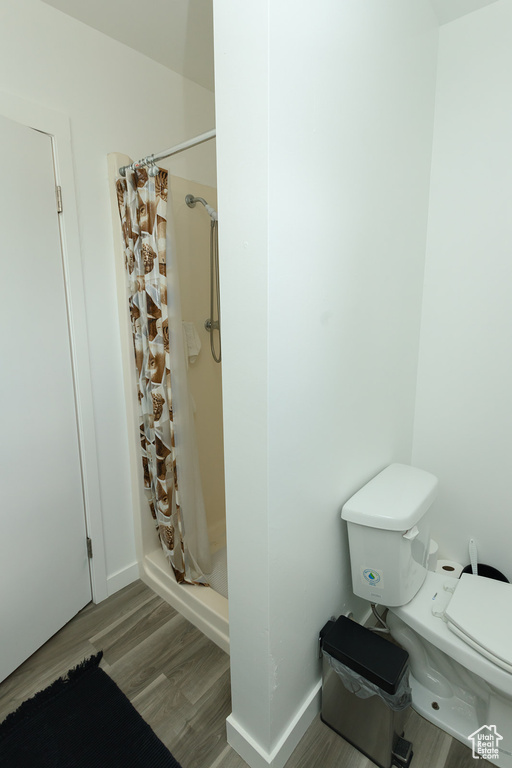 Bathroom featuring a shower with shower curtain, toilet, and hardwood / wood-style floors