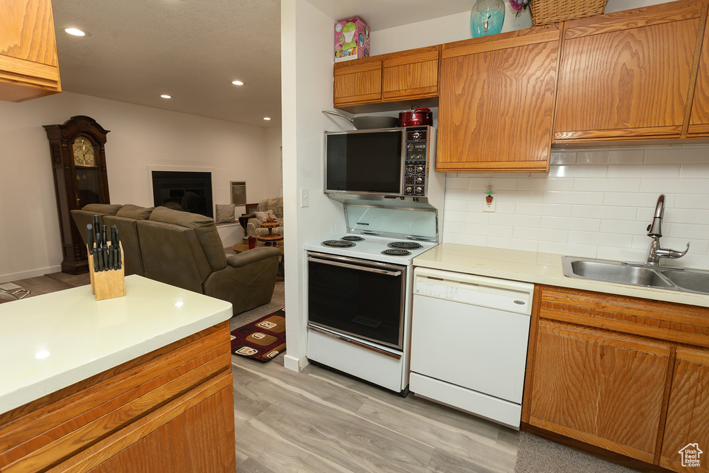 Kitchen featuring white appliances, light hardwood / wood-style floors, backsplash, and sink
