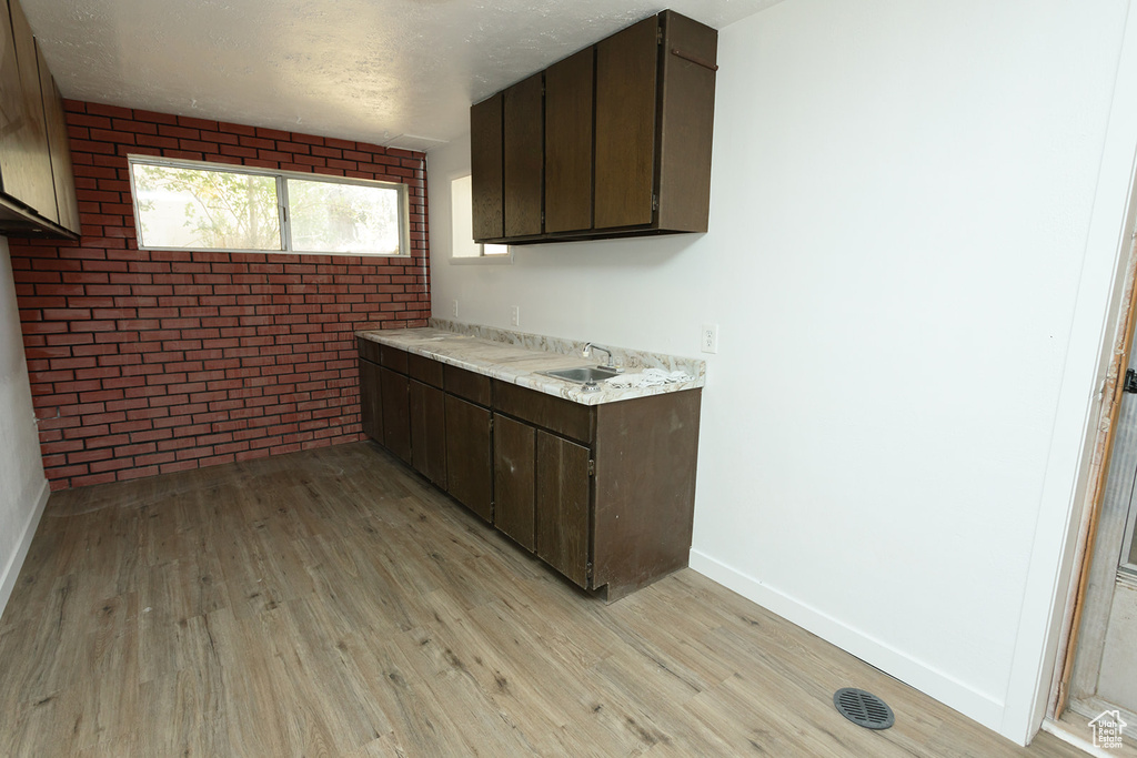 Kitchen with brick wall, light hardwood / wood-style flooring, and dark brown cabinets