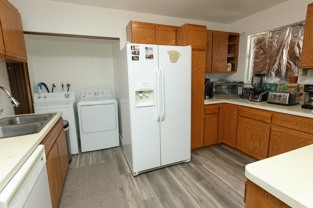 Kitchen with white appliances, light wood-type flooring, washing machine and dryer, and sink