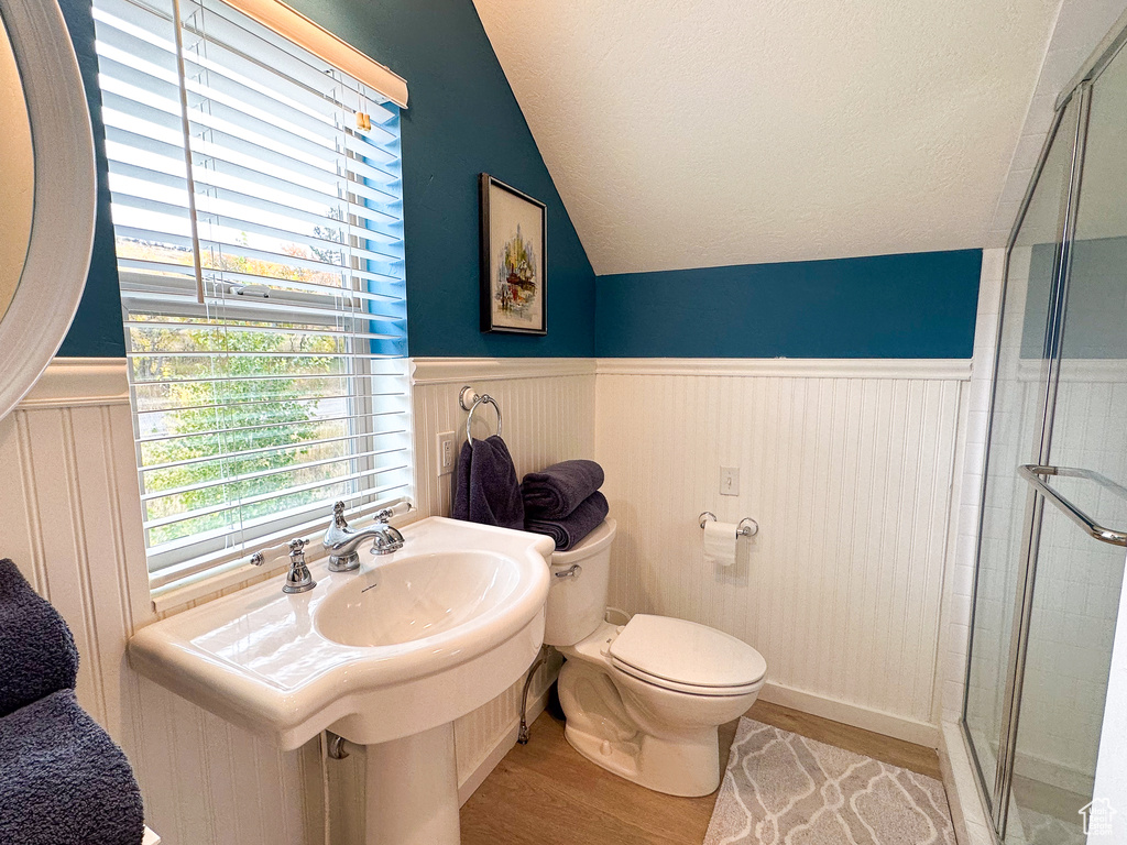 Bathroom featuring a shower with shower door, vaulted ceiling, toilet, and hardwood / wood-style flooring