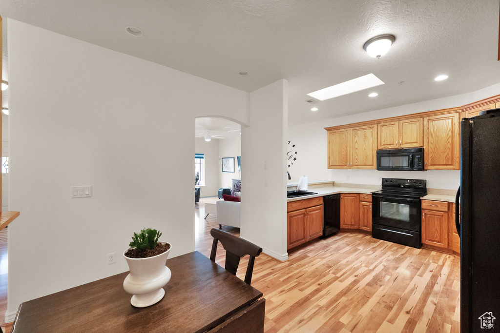 Kitchen featuring light wood-type flooring, black appliances, ceiling fan, and a skylight