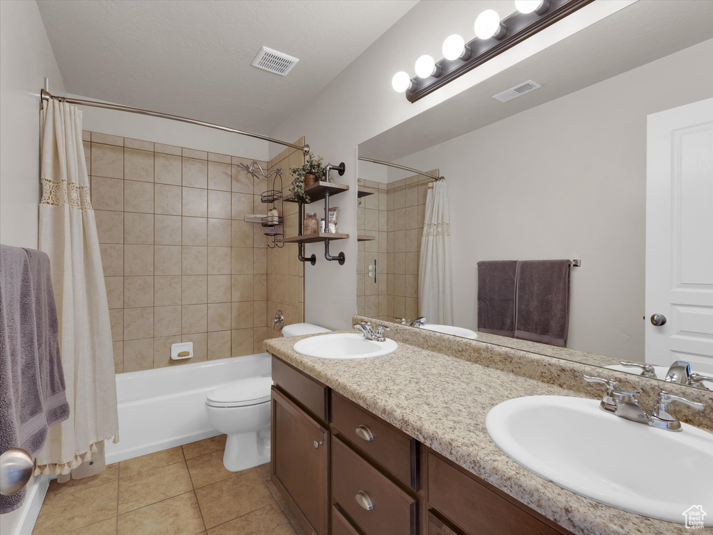 Full bathroom with toilet, double vanity, tile floors, and shower / tub combo
