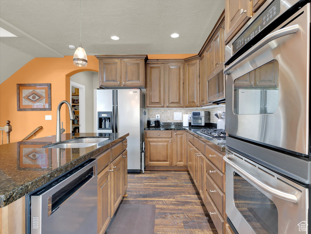Kitchen featuring dark wood-type flooring, stainless steel appliances, backsplash, an island with sink, and sink