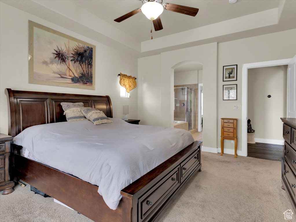 Carpeted bedroom with a tray ceiling, ceiling fan, and ensuite bath