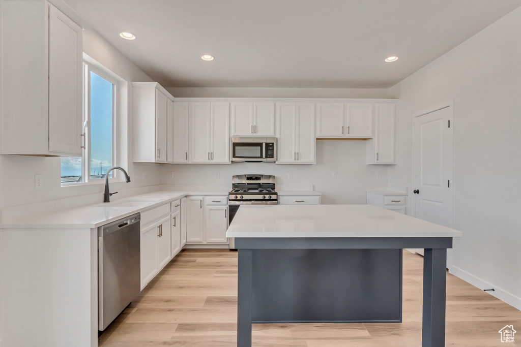 Kitchen featuring light wood-type flooring, stainless steel appliances, white cabinetry, sink, and a center island