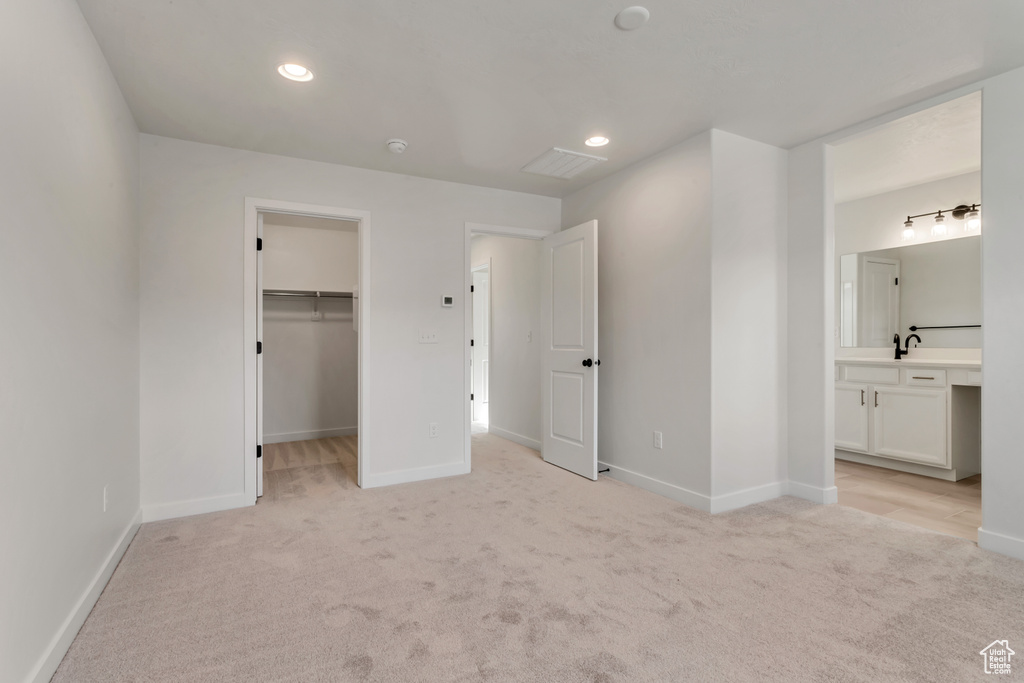 Unfurnished bedroom with a spacious closet, light colored carpet, ensuite bathroom, and a closet