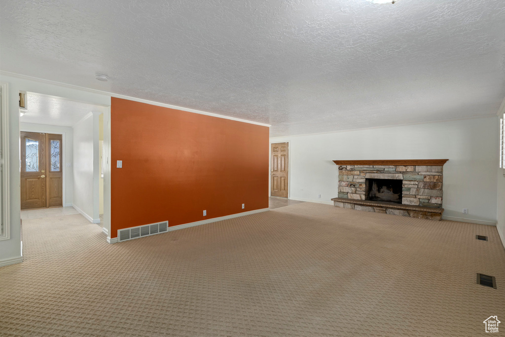 Unfurnished living room featuring light colored carpet, a stone fireplace, a textured ceiling, and crown molding