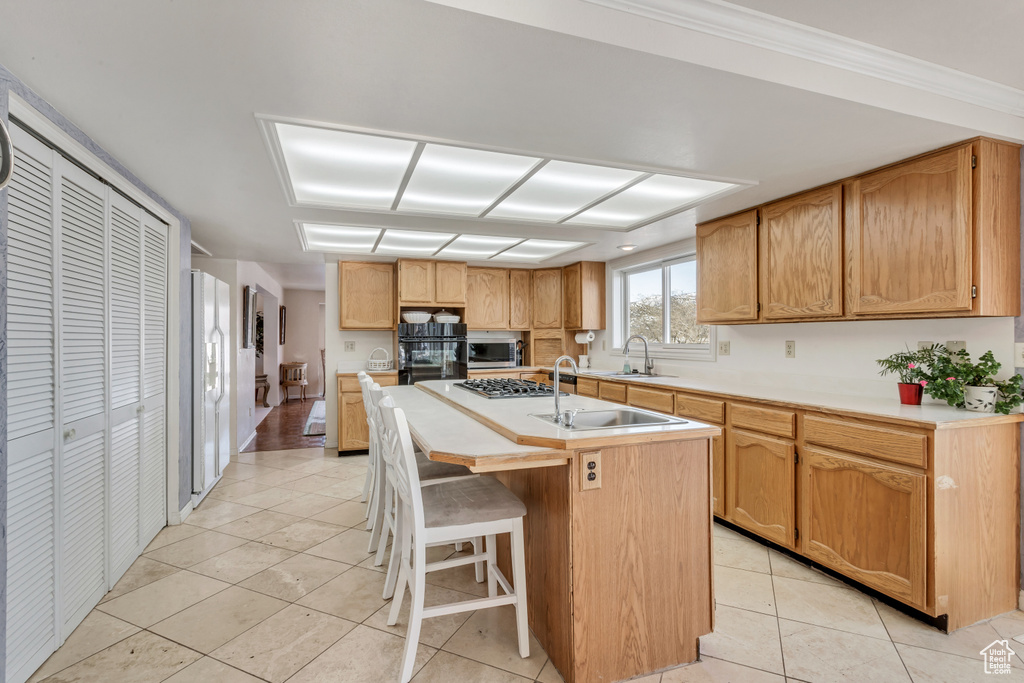 Kitchen featuring ornamental molding, a breakfast bar, light tile flooring, appliances with stainless steel finishes, and an island with sink