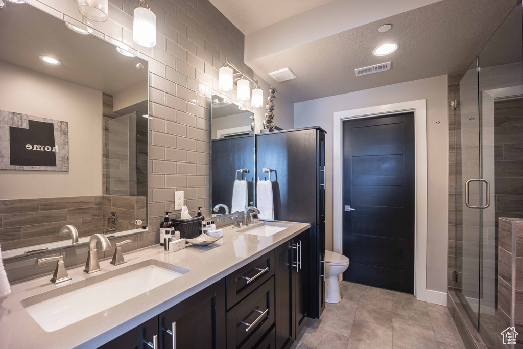 Bathroom featuring walk in shower, toilet, tile walls, tasteful backsplash, and double sink vanity