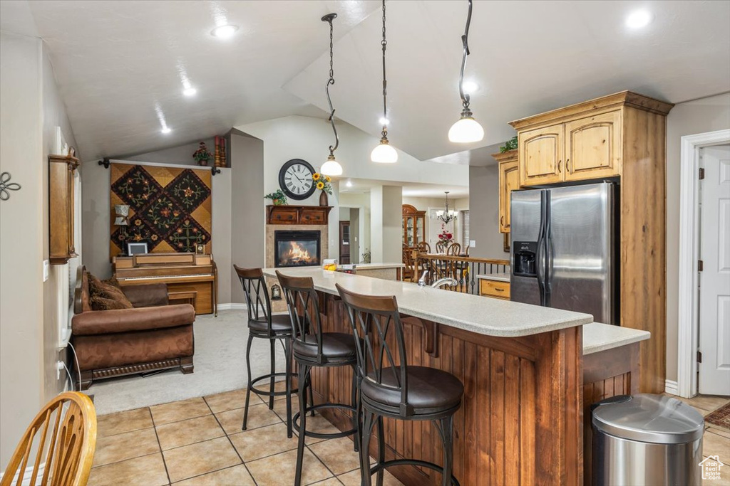 Kitchen with a kitchen bar, stainless steel refrigerator with ice dispenser, vaulted ceiling, decorative light fixtures, and light tile floors