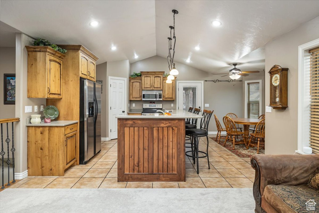 Kitchen featuring vaulted ceiling, light tile floors, stainless steel appliances, ceiling fan, and decorative light fixtures