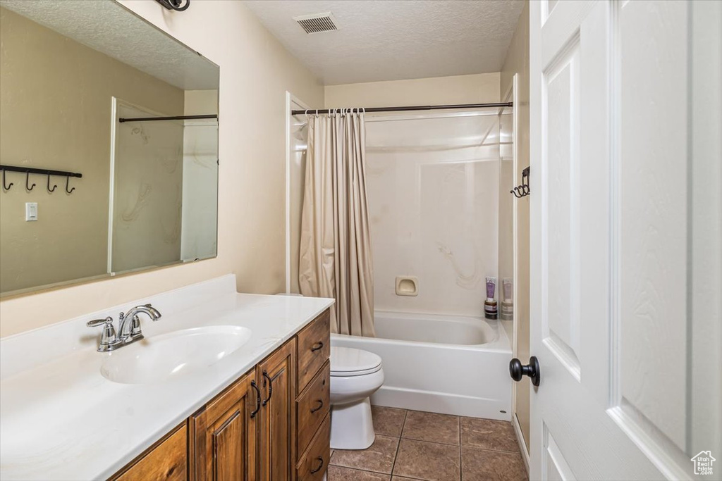 Full bathroom with vanity, shower / bath combo, a textured ceiling, toilet, and tile floors