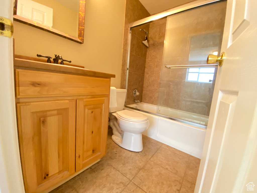Full bathroom featuring combined bath / shower with glass door, vanity, tile flooring, and toilet