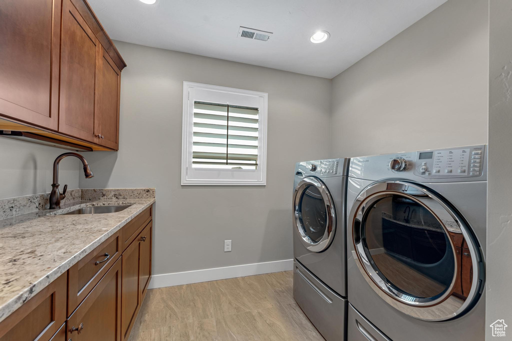 Laundry area featuring light hardwood / wood-style flooring, sink, washing machine and dryer, and cabinets