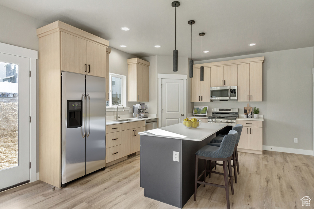 Kitchen with a center island, a kitchen breakfast bar, pendant lighting, light wood-type flooring, and stainless steel appliances