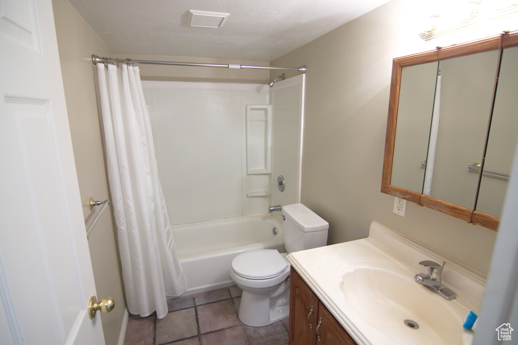 Full bathroom with a textured ceiling, vanity, shower / bath combination with curtain, toilet, and tile flooring