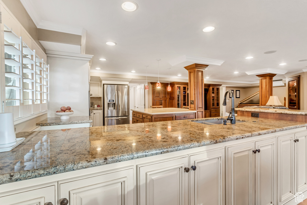Kitchen with stainless steel fridge, light stone counters, ornate columns, sink, and decorative light fixtures