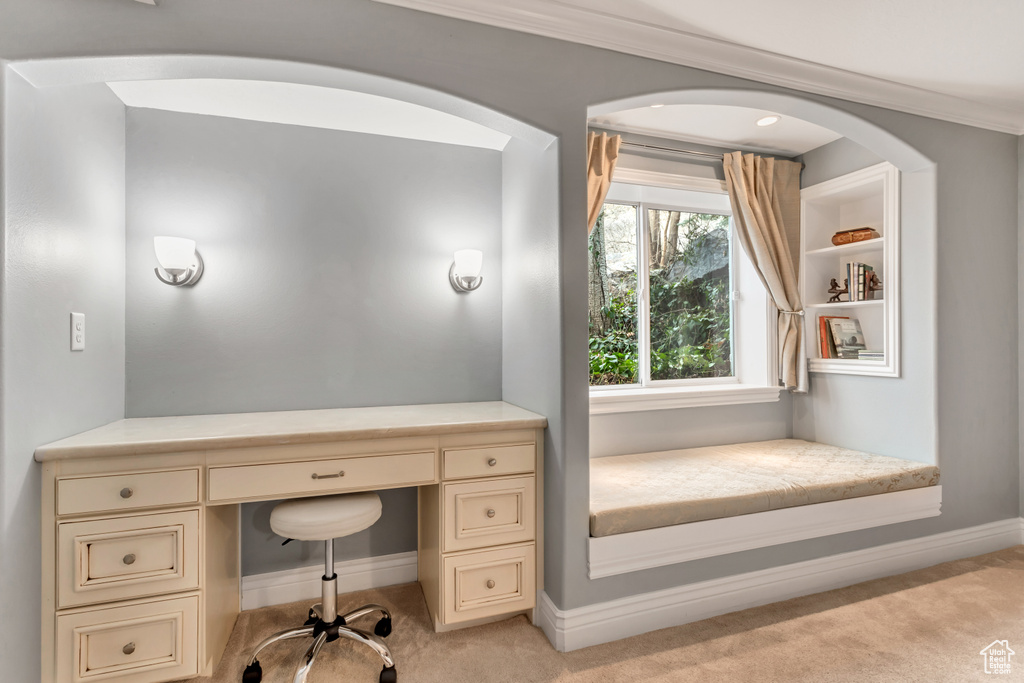 Home office featuring ornamental molding, light colored carpet, and built in desk