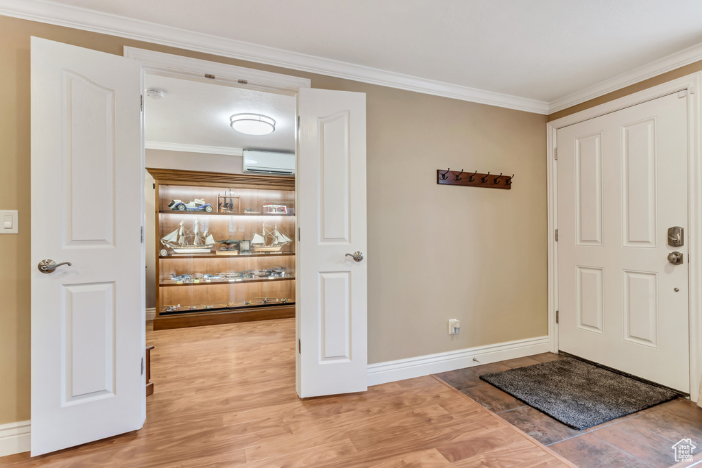 Entryway featuring ornamental molding, light wood-type flooring, and a wall unit AC