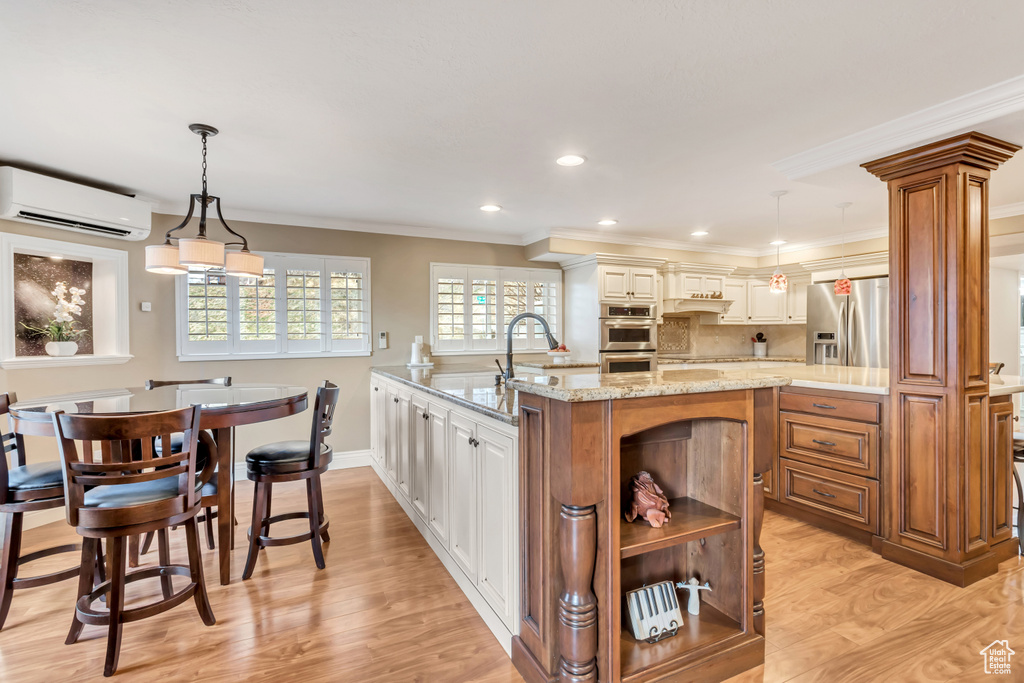 Kitchen featuring light hardwood / wood-style floors, a center island with sink, hanging light fixtures, stainless steel appliances, and a wall mounted air conditioner