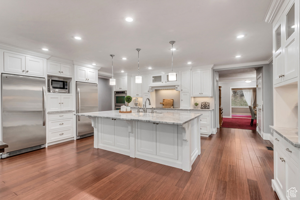 Kitchen featuring white cabinetry, built in appliances, a kitchen island with sink, and wood-type flooring