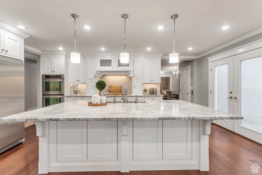 Kitchen featuring hardwood / wood-style floors, pendant lighting, french doors, stainless steel appliances, and white cabinets