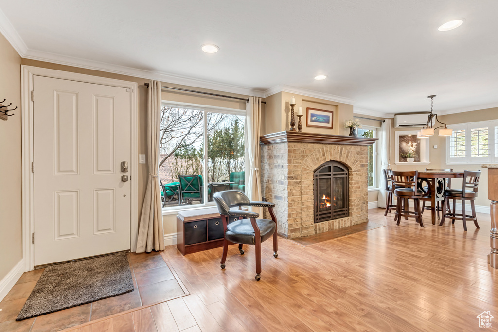 Entryway featuring ornamental molding, light wood-type flooring, a fireplace, and a wall mounted air conditioner