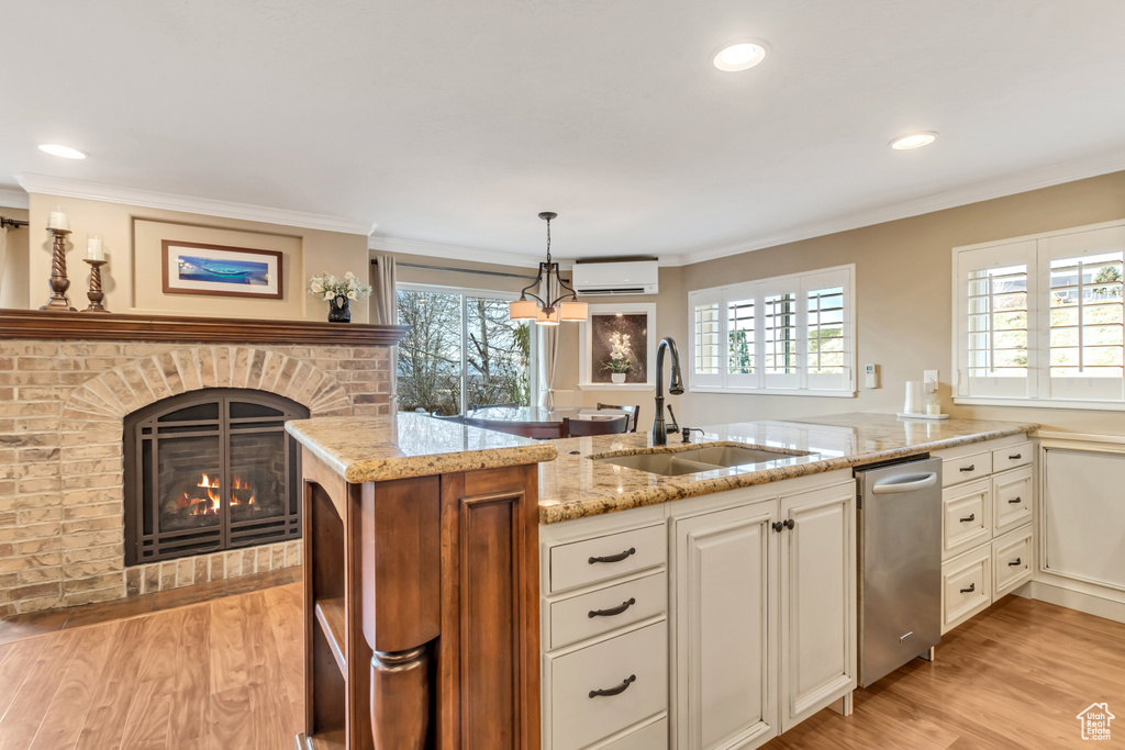 Kitchen featuring dishwasher, a fireplace, sink, light stone counters, and decorative light fixtures