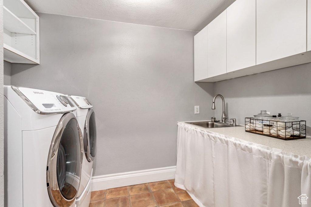 Clothes washing area with washer and dryer, sink, light tile floors, and cabinets