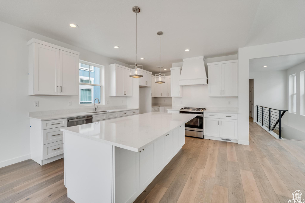 Kitchen with premium range hood, stainless steel appliances, white cabinets, a kitchen island, and light hardwood / wood-style flooring