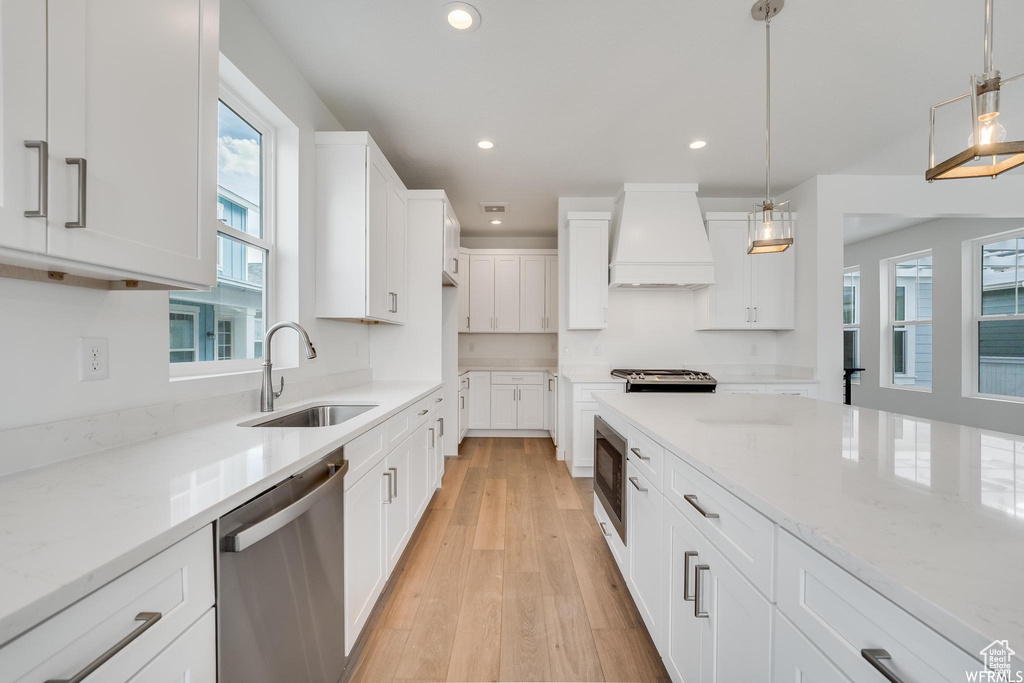Kitchen with hanging light fixtures, white cabinetry, sink, premium range hood, and appliances with stainless steel finishes