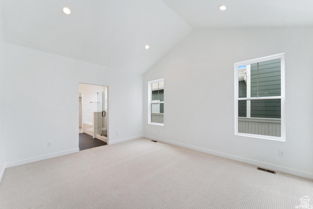 Unfurnished bedroom with multiple windows, high vaulted ceiling, light carpet, and ensuite bath